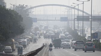 Komuter berjalan di sepanjang jalan di tengah kabut asap tebal di New Delhi, India, pada (16/11/2021). [MONEY SHARMA / AFP]