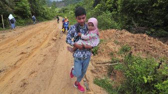 Seorang pelajar menggendong adiknya saat melintasi jalan rusak di Desa Meribung, Limun, Sarolangun, Jambi, Kamis (18/11/2021). [ANTARA FOTO/Wahdi Septiawan]