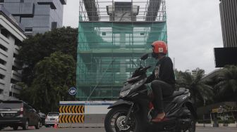 Pengendara sepeda motor berhenti di samping tugu jam yang dipasang perancah di Jalan MH. Thamrin, Jakarta, Jumat (19/11/2021). [Suara.com/Angga Budhiyanto]
