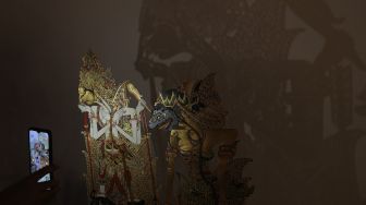 Pengunjung menyinari koleksi wayang menggunakan lampu saat pameran wayang bertema &#039;Wayang Rupa Kita&#039; di Bentara Budaya, Palmerah, Jakarta, Sabtu (20/11/2021). [Suara.com/Angga Budhiyanto]