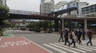 Sejumlah pejalan kaki berjalan di dekat proyek revitalisasi Jembatan Penyeberangan Orang (JPO) Sudirman di Jakarta, Selasa (23/11/2021). [Suara.com/Angga Budhiyanto]