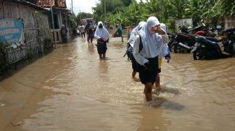 Sejumlah pelajar melintasi genangan air saat terjadi banjir di Kelurahan Pesurungan, Tegal, Jawa Tengah, Selasa (23/11/2021). ANTARA FOTO/Oky Lukmansya