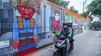 Pengendara motor melintas di depan mural dengan tema Jakarta di Kebayoran Lama, Jakarta Selatan, Jumat (26/11/2021). [Suara.com/Alfian Winanto]