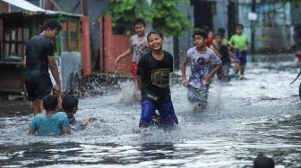 Anak - anak bermain banjir di Jalan Wijaya Timur, Petogogan, Jakarta Selatan, Jumat (26/11/2021). [Suara.com/Alfian Winanto]