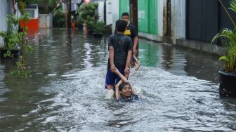 Anak - anak bermain banjir di Jalan Wijaya Timur, Petogogan, Jakarta Selatan, Jumat (26/11/2021). [Suara.com/Alfian Winanto]