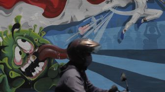 Pengendara sepeda motor melintas di depan mural bertema COVID-19 di Jakarta, Jumat (26/11/2021). [Suara.com/Angga Budhiyanto]