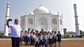 Pengusaha India Anand Prakash Chouksey (kiri) berpose bersama anak-anak sekolah yang berkunjung di depan replika Taj Mahal, Burhanpur, negara bagian Madhya Pradesh, India, pada (25/11/2021). [UMA SHANKAR MISHRA / AFP]
