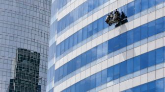 Pekerja membersihkan dan melakukan perawatan bagian kaca luar salah satu gedung bertingkat di kawasan Jakarta Selatan, Minggu (28/11/2021). [Suara.com/Alfian Winanto]