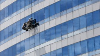 Pekerja membersihkan dan melakukan perawatan bagian kaca luar salah satu gedung bertingkat di kawasan Jakarta Selatan, Minggu (28/11/2021). [Suara.com/Alfian Winanto]