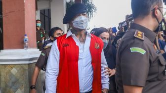 Musisi I Gede Ari Astina atau Jerinx SID berjalan keluar mengenakan rompi tahanan berwarna merah usai menjalani pemeriksaan di Kejaksaan Negeri Jakarta Pusat, Rabu (1/12/2021). [Suara.com/Alfian Winanto]