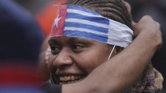 Massa aksi membantu memasangkan ikat kepala bergambar bendera Papua Barat kepada rekannya saat melakukan unjuk rasa memperingati 60 tahun deklarasi kemerdekaan Papua Barat di kawasan Patung Kuda Arjuna Wiwaha, Jakarta, Rabu (1/12/2021). [Suara.com/Angga Budhiyanto]