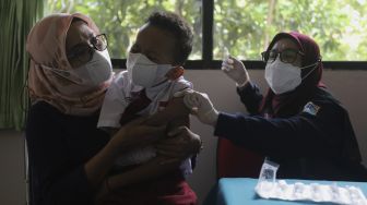 Orang tua menenangkan anaknya yang akan mendapatkan vaksin COVID-19 kepada pelajar di SDN 04 Cilandak Barat, Jakarta, Selasa (14/12/2021). [Suara.com/Angga Budhiyanto]