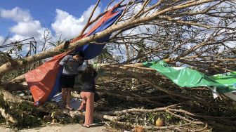 Turis lokal berlindung di bawah pohon tumbang di luar bandara di kota Del Carmen, Pulau Siargao, Provinsi Surigao del Norte, Filipina, pada (19/12/2021). [ROEL CATOTO / AFP]