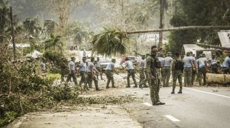 Polisi berjaga-jaga sementara rekan-rekannya membersihkan jalan dari puing-puing di Kota Surigao, Provinsi Surigao del Norte, Filipina, pada (19/12/2021). [FERDINANDH CABRERA / AFP]