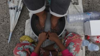 Seorang anak bersiap membasuh kaki ibunya saat acara Cuci Kaki Ibu Massal di Kelurahan Duri Pulo, Gambir, Jakarta, Rabu (22/12/2021). [Suara.com/Angga Budhiyanto]