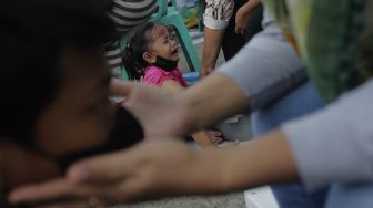 Seorang anak menangis saat membasuh kaki ibunya dalam acara Cuci Kaki Ibu Massal di Kelurahan Duri Pulo, Gambir, Jakarta, Rabu (22/12/2021). [Suara.com/Angga Budhiyanto]