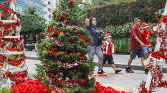 Warga melintas didepan hiasan pohon yang terpajang di Kawasan Bundaran HI, Jakarta Pusat, Sabtu (25/12/2021). [Suara.com/Alfian Winanto]