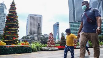 Warga melintas didepan hiasan pohon yang terpajang di Kawasan Bundaran HI, Jakarta Pusat, Sabtu (25/12/2021). [Suara.com/Alfian Winanto]