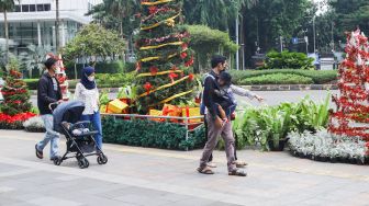 Warga melintas didepan hiasan pohon yang terpajang di Kawasan Bundaran HI, Jakarta Pusat, Sabtu (25/12/2021). [Suara.com/Alfian Winanto]