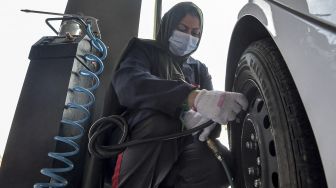 Seorang mekanik perempuan Saudi mengisi udara ban kendaraan di bengkel perbaikan dan servis di kota pesisir Laut Merah, Arab Saudi, Jeddah, pada (27/12/2021). [AMER HILABI / AFP]