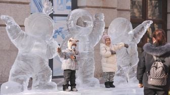 Anak-anak bermain dengan patung esdi Harbin Ice and Snow World, Harbin, Provinsi Heilongjiang, China, pada (28/12/2021). [AFP]