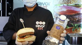 Seorang pria memegang potongan setengah patty nabati dengan rasa daging yang dibuat dan dimasak oleh robot di kota pesisir Israel, Herzliya, pada (28/12/2021). [JACK GUEZ / AFP]