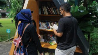 Pengunjung membaca buku di perpustakaan mini di Taman Suropati, Jakarta, Minggu (9/1/2022). [Suara.com/Septian]