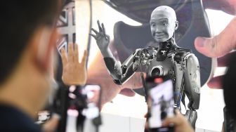 Para peserta berfoto dan berinteraksi dengan robot Humanoid Engineered Arts Ameca dengan kecerdasan buatan yang diperagakan selama Consumer Electronics Show (CES) di Las Vegas, Nevada, Amerika Serikat, pada (5/1/2022). [PATRICK T. FALLON / AFP]
