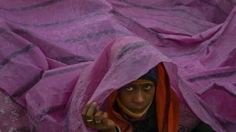 Seorang peziarah menggunakan lembaran plastik untuk berlindung dari hujan di Gangasagar Mela pada kesempatan Makar Sankranti di Pulau Sagar, India, pada (14/1/2022). [DIBYANGSHU SARKAR / AFP]