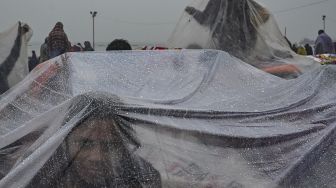 Peziarah Hindu menggunakan lembaran plastik untuk berlindung dari hujan setelah berenang suci di pertemuan Sungai Gangga dan Teluk Benggala selama Gangasagar Mela pada kesempatan Makar Sankranti di Pulau Sagar, India, pada (14/1/2022). [DIBYANGSHU SARKAR / AFP]