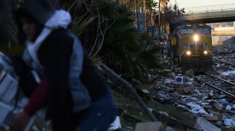 Seseorang membawa barang-barang yang dikumpulkan dari rel kereta api saat lokomotif Union Pacific melewati rel yang dipenuhi ribuan kotak terbuka dan paket yang dicuri dari kontainer pengiriman kargo di pusat Kota Los Angeles, California, Amerika Serikat, pada (14/1/2022). [PATRICK T. FALLON / AFP]