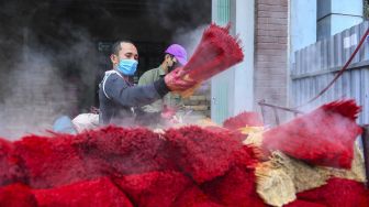 Seorang pekerja mewarnai dupa di sebuah bengkel di Desa Quang Phu Cau, Hanoi, Vietnam, pada (12/1/2022). [NHAC NGUYEN / AFP]