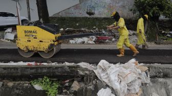 Petugas Suku Dinas Bina Marga Jakarta Pusat memperbaiki jalan ambles di Jalan Inspeksi Kali Ciliwung, Kenari, Kecamatan Senen, Jakarta, Rabu (19/1/2022). [Suara.com/Angga Budhiyanto]
