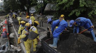 Petugas Suku Dinas Bina Marga Jakarta Pusat memperbaiki jalan ambles di Jalan Inspeksi Kali Ciliwung, Kenari, Kecamatan Senen, Jakarta, Rabu (19/1/2022). [Suara.com/Angga Budhiyanto]