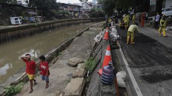 Dua orang anak berjalan di samping perbaikan jalan ambles di Jalan Inspeksi Kali Ciliwung, Kenari, Kecamatan Senen, Jakarta, Rabu (19/1/2022). [Suara.com/Angga Budhiyanto]