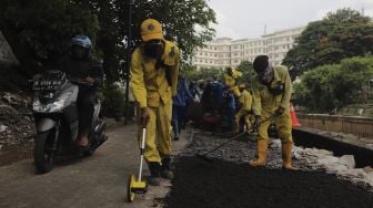 Petugas Suku Dinas Bina Marga Jakarta Pusat memperbaiki jalan ambles di Jalan Inspeksi Kali Ciliwung, Kenari, Kecamatan Senen, Jakarta, Rabu (19/1/2022). [Suara.com/Angga Budhiyanto]