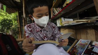 Seorang anak membaca buku di pustaka mini Bale Buku di Kelurahan Dukuh, Kramat Jati, Jakarta, Kamis (20/1/2022). [Suara.com/Angga Budhiyanto]