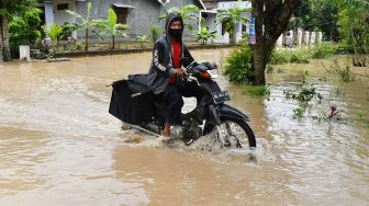 Pengendara sepeda motor menerobos jalan yang terendam banjir di Kabupaten Madiun, Jawa Timur, Kamis (20/1/2022). ANTARA FOTO/Siswowidodo