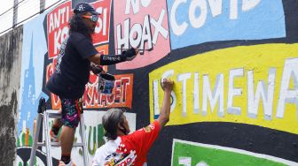 Pekerja seni membuat mural di kawasan Palmerah, Jakarta Pusat, Minggu (23/1/2022). [Suara.com/Alfian Winanto]