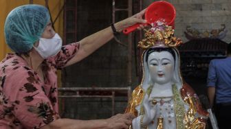 Petugas membersihkan patung dewa di Vihara Amurva Bhumi, Jakarta, Selasa (25/1/2022). [Suara.com/Septian]