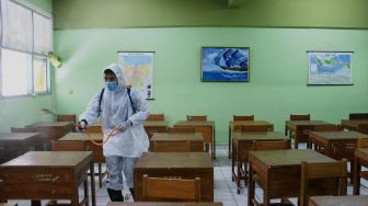 Petugas Palang Merah Indonesia (PMI) menyemprotkan cairan disinfektan di SMA Negeri 66 Jakarta, Jumat (28/1/2022). [Suara.com/Septian]