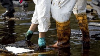 Pekerja membersihkan tumpahan minyak mentah di Pantai Mae Ram Phueng, menyusul tumpahan yang disebabkan oleh kebocoran pipa bawah laut milik Star Petroleum Refining Public Company Limited (SPRC) di Rayong, Thailand, Sabtu (29/1/2022). [JACK TAYLOR / AFP]