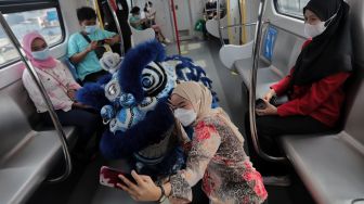 Seorang penumpang berswafoto dengan barongsai di dalam gerbong LRT, Jakarta, Selasa (1/2/2022). [Suara.com/Angga Budhiyanto]