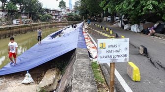 Warga melintas di samping jalan yang amblas di Jalan Inspeksi Kali Ciliwung, Jatinegara, Jakarta Timur, Jumat (4/2/2022). [Suara.com/Alfian Winanto]