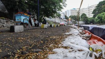 Warga melintas di samping jalan yang amblas di Jalan Inspeksi Kali Ciliwung, Jatinegara, Jakarta Timur, Jumat (4/2/2022). [Suara.com/Alfian Winanto]