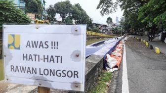 Warga melintas di samping jalan yang amblas di Jalan Inspeksi Kali Ciliwung, Jatinegara, Jakarta Timur, Jumat (4/2/2022). [Suara.com/Alfian Winanto]