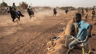 Seorang anak duduk diatas sepedanya saat menyaksikan pertandingan balap kuda di Kota Ouagadougou, Burkina Faso, Senin (30/1/2022). [Photo by JOHN WESSELS / AFP]