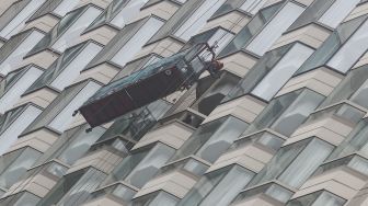 Pekerja membersihkan jendela gedung bertingkat di Kawasan Bundaran Hotel Indonesia (HI), Jakarta Pusat, Sabtu (12/2/2022). [Suara.com/Alfian Winanto]