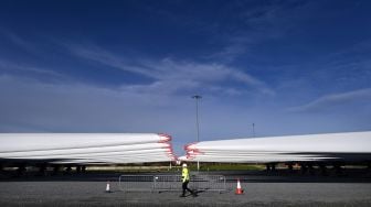 Seorang pegawai melintas di depan Bilah turbin angin yang disimpan di dermaga dan siap untuk dikirim di pabrik bilah Siemens Gamesa di Hull, Inggris, Jumat (28/1/2022). [Paul ELLIS / AFP]