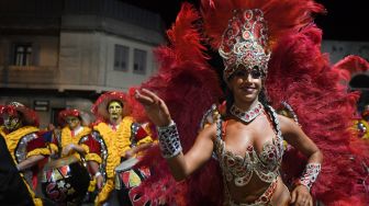 Para penabuh drum dan penari yang dikenal sebagai 'komparsa' bersaing dengan dengan memainkan musik dan tarian tradisional 'candombe' saat festival 'Las Llamadas' di Montevideo, Uruguay, Kamis (10/2/2022). [PABLO PORCIUNCULA / AFP]